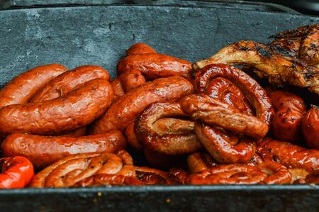 Close up. Sausages are grilled and stacked in a large cast-iron pan. Snacks in the park at the...
