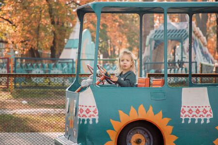 Little blond girl rides on attraction. Autumn park on the background.の写真素材