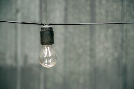 A light bulb on the horizontal wire after the autumn rain. Element of a street garland. In the background a gray iron wall.の写真素材
