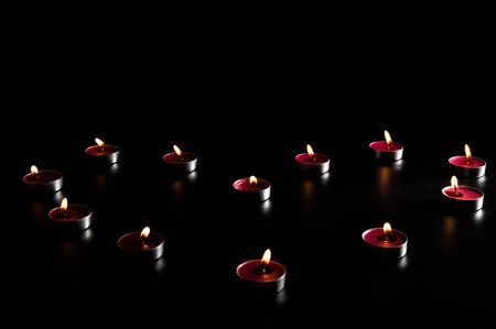 Close up. Valentine's Day decoration. Red burning candles laid out in the shape of a heart. Black background, low key. Copy space.の写真素材