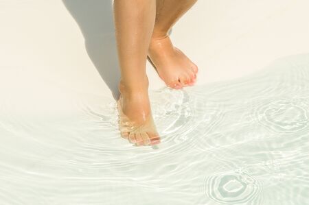Rest with the child. The child's legs neatly enter the water in shallow water in the children's pool with a white rubber coating. Close up.の写真素材