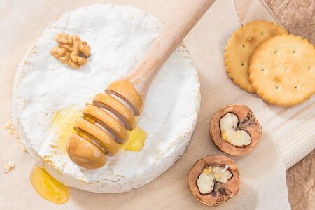 Camembert cheese with crackers, walnuts and honey. In the background a wooden board and a white parchment.の写真素材