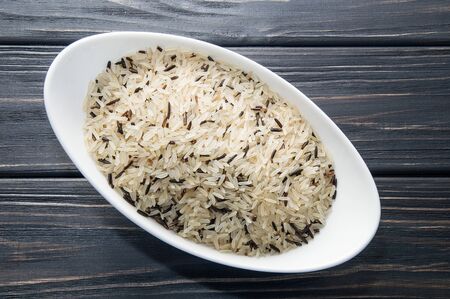Top view, close up, macro. White oblong bowl filled with wild rice. Dark wooden background.の写真素材