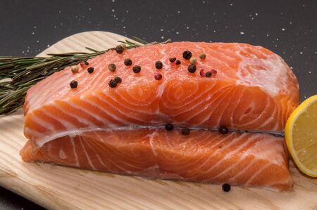Close up, macro. Ingredients. Fresh fish. Salmon steak surrounded by lemon, spices and herbs on a wooden board. Black background.の写真素材