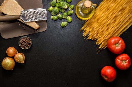 Flat lay, space for text. Ingredients for italian pasta. Spaghetti, tomatoes, oil, onion, parmezan on black background.の写真素材