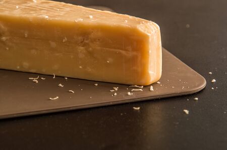 Close up, macro. Italian cuisine. A chunk of parmesan cheese on a brown board. Black background.の写真素材