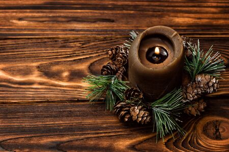 Close up, macro. A lit brown candle is decorated with a spruce branch. Brown wooden boards on the background. Copy space to the left.の写真素材