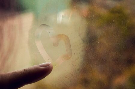 Close up. The girl draws a heart on the fogged glass. Golden rainy autumn on the background.