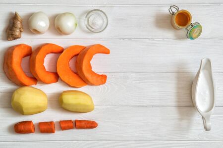 Close up, top view. Peeled lined ingredients for pumpkin cream soup: carrot, pumkin, onion, potatoes. Plant-based food on the white wooden background. Copy space.の写真素材