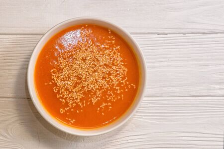 Close up, top view. White bowl with bright pumpkin cream soup, sprinkled with sesame seeds. Plant-based food on the white wooden background. Copy space.の写真素材