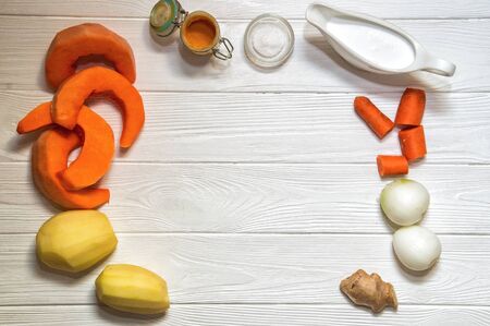 Close up, top view. Peeled ingredients for pumpkin cream soup. Salt, curcuma and sauceboat with cream. Plant-based food on the white wooden background. Copy space.の写真素材