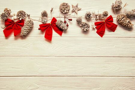 Top view, flat lay. Christmas textural wooden background. Traditional stylized garland with small and big fir cones, red bows and stars. Warm tones. Copy space below.の写真素材