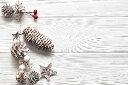 Top view, flat lay. Christmas woden background. Traditional garland, vertical to the boards, with red and white berries, snowy fir cones and stars. Copy space on the right.の写真素材
