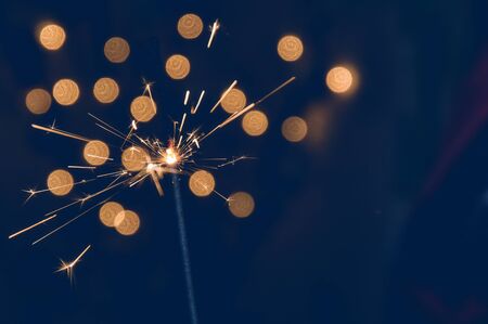 Macro, close up. Magic burning sparkler. Dark blue background with blurred lights of Christmas garland. Copy space on the right.の写真素材