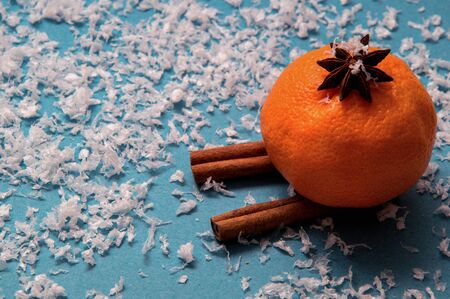 Close up, macro. Orange mandarine in aniseed hat skiing out of cinnamon. Deep blue background with artificial snow. Copy space.の写真素材