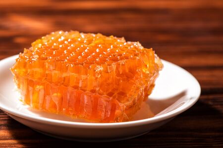 Macro, close up. Rustic food. Bright orange honeycombs on a snow-white saucer. Brown wooden background. Copy space.の写真素材