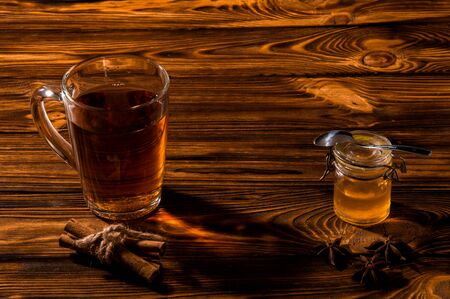 Close up. Black aromatic tea in a glass transparent cup. Glass jar with gold honey on a rustic brown wooden table. Copy space.の写真素材