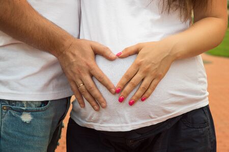Waiting for the child. Pregnant girl and future father make heart with hands on tummy background.の写真素材