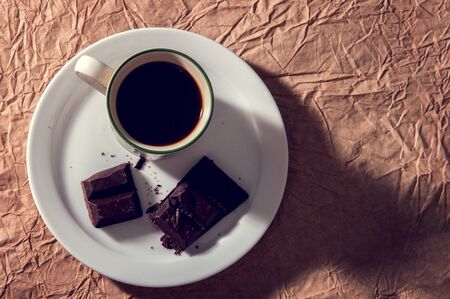 Cup of black coffee with a pieces of dark chocolate. Flat lay on brown textural paper background. Vintage tintingの写真素材