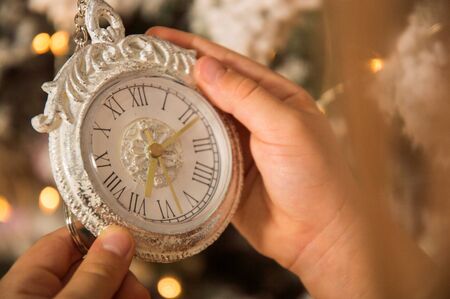 Close up, macro. Christmas concept. Children's hands are holding a vintage white clock. Against the...