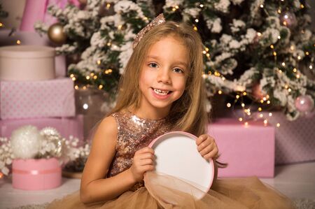 Close up, macro. Christmas concept. A beautiful little girl in an elegant dress sits and smiles while holding a pink gift box.の写真素材