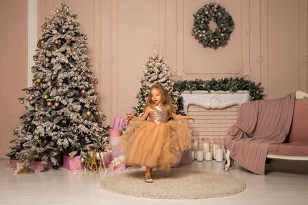 Close up. Beautiful little girl dancing in a golden dress on a background of the Christmas location. Christmas concept.の写真素材
