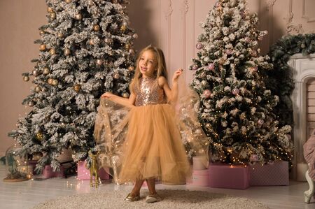 Close up. Christmas concept. A beautiful child in a golden elegant dress exquisitely dances in a festively decorated room.の写真素材
