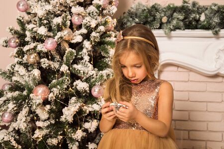 Close up. Christmas concept. A little girl in a golden dress is waiting, looking at the clock near the Christmas tree.の写真素材