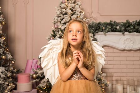 Close up. Christmas concept. A little girl in the image of a Christmas angel with wings dreamily folded her arms and looks up.の写真素材