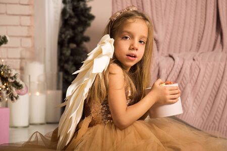 Close up. Christmas concept. A little girl in a golden dress holding a gift box.の写真素材