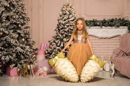 Close up. Christmas concept. A little girl in an elegant dress is surrounded by large decorative cones near the festive Christmas tree.の写真素材