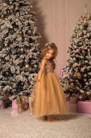 Close up. Christmas concept. A beautiful girlie in a golden elegant dress exquisitely dances in a festively decorated room.の写真素材