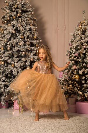 Close up. Beautiful little girl dancing in a golden dress on a background of the Christmas tree. Christmas concept.の写真素材