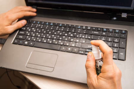 Close up. Male hand disinfect the laptop keyboard. Hygiene during the coronavirus pandemic.