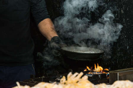 Close up. Italian street food. The cook heats up a pot of water to cook the tagliatelle over the fire. Night.の写真素材