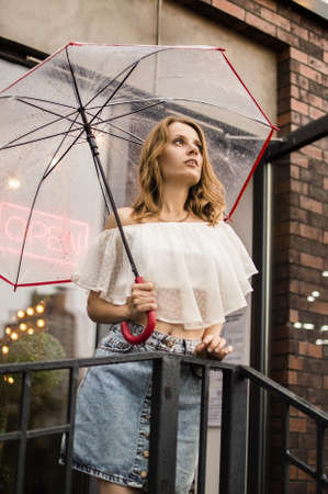 Close up. Portrait of a girl under a transparent umbrella in the rain. Loft style building in the background.の写真素材