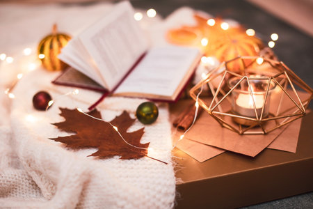 Close up. December evening. An open book on a beige blanket, next to pumpkin and leaves, warm lights of a garland.の写真素材