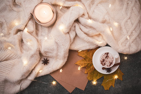 Close up. Top view, flat lay. Autumn-winter composition in brown-beige colors in the hygge style. Cozy knitted blanket, Christmas garland, small pumpkins, a cup of hot cappuccino with spices.の写真素材