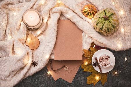 Close up. Sheets of brown retro paper, knitted blanket, garland, small pumpkins, a cup of hot cappuccino. Copy space.の写真素材