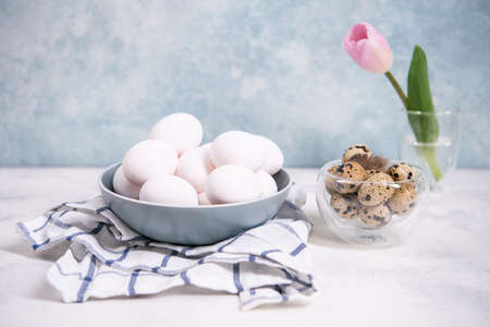 A bunch of brown quail eggs and a bunch of white chicken eggs, on a checkered napkin. Nearby is a...