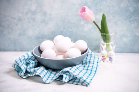 Close up. A bunch of white chicken eggs in a blue bowl. Farm product. Nearby are pink tulip. White and blue pastel background. Preparing for Easter.の写真素材