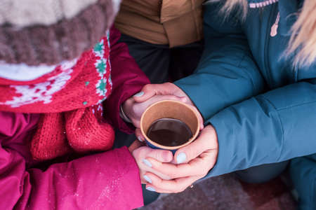 Close up. Mom and daughter hold a hot cup of coffee in their palms. Family on a walk together in winter.の写真素材