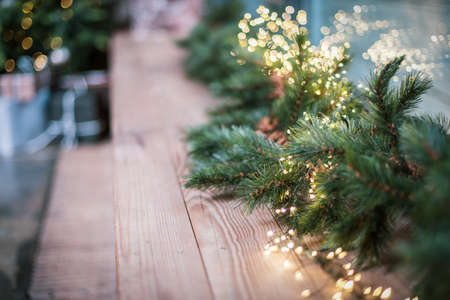 Close up. Spruce branches with a glowing Christmas garland decorate the windowsill. Christmas tree and gifts on the background.の写真素材
