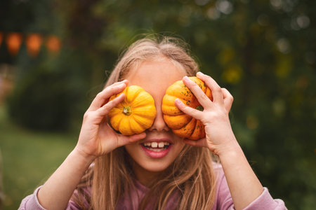Close up. Portrait of a child girl on Pumpkin farm. Long-haired 8 years old girl smiles and covers his eyes with small pumpkins.の写真素材