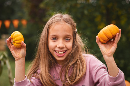 Close up. Portrait of a child girl on Pumpkin farm. Long-haired 8 years old girl smiles and holds tiny pumpkins.の写真素材