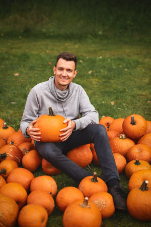 Portrait of smiling man holding big pumpkin at pumpkin farm. Vertical oriented.の写真素材