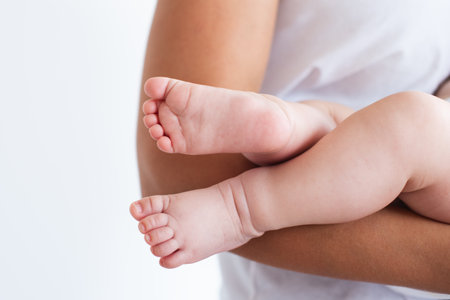 Close up, macro. The little legs of the baby with tiny fingers on the hands of the mother. White background.の写真素材
