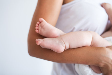 Close up, macro. Small legs of the baby in the arms of the mother. Simple photo, white background.の写真素材