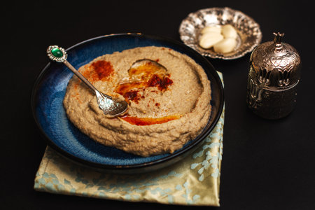 Close-up. Homemade Baba Ganush on a dark blue plate surrounded by silverware. Black background.の写真素材