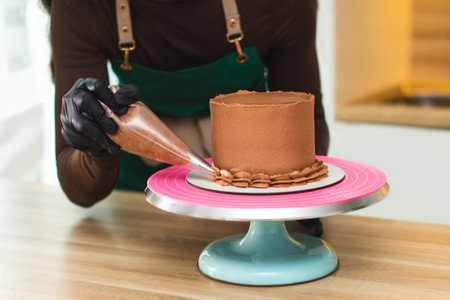 Close-up. The process of a confectioner applying chocolate cream from a pastry bag onto a cake.の写真素材